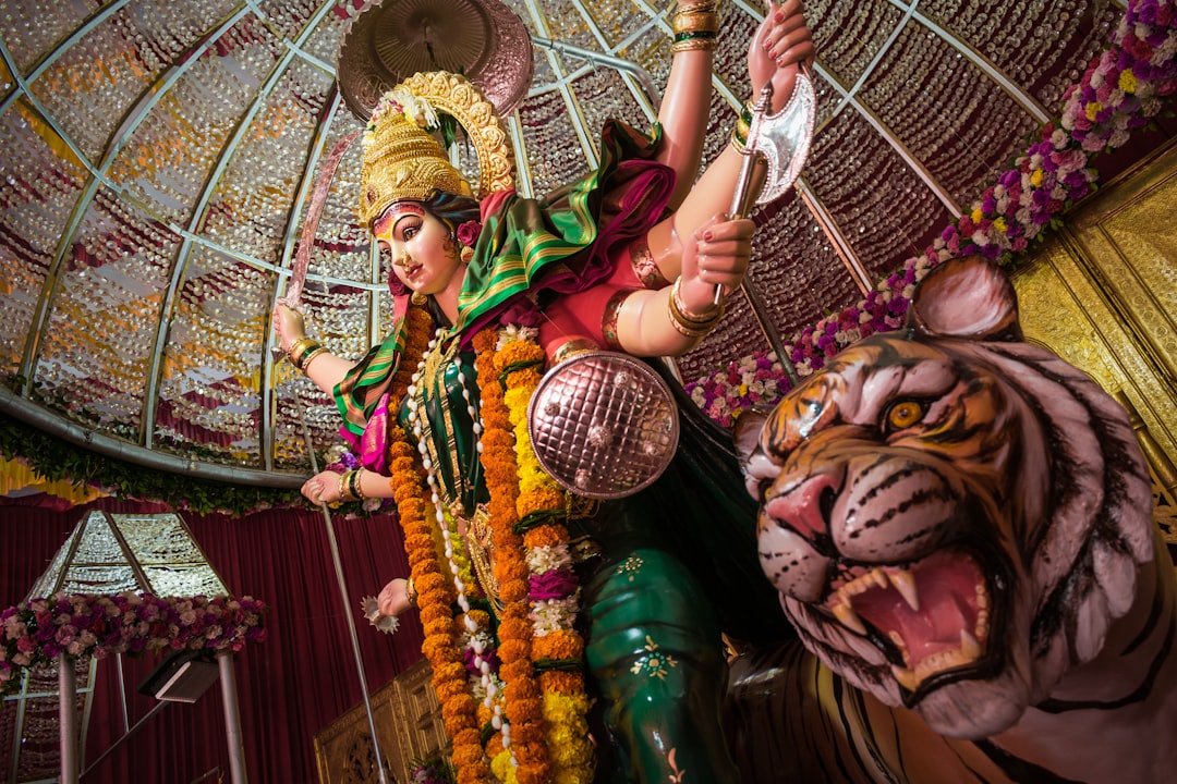 An idol of Maa Durga Devi at a temple in Mumbai, India during Navratri 2019 by Hispanic Month woman in green and brown traditional dress holding brown woven basket