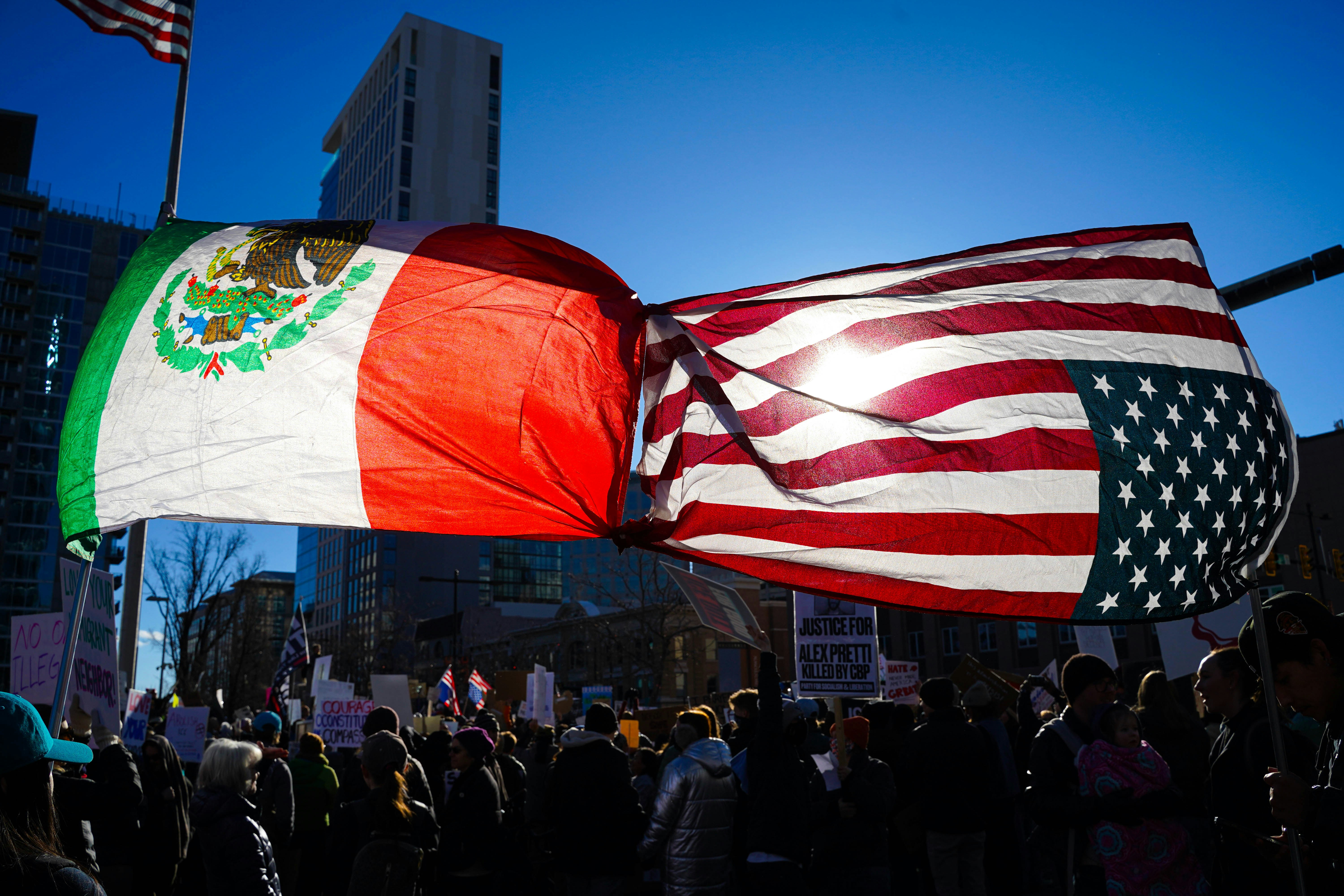 Mexican and american flags waving together above crowd.