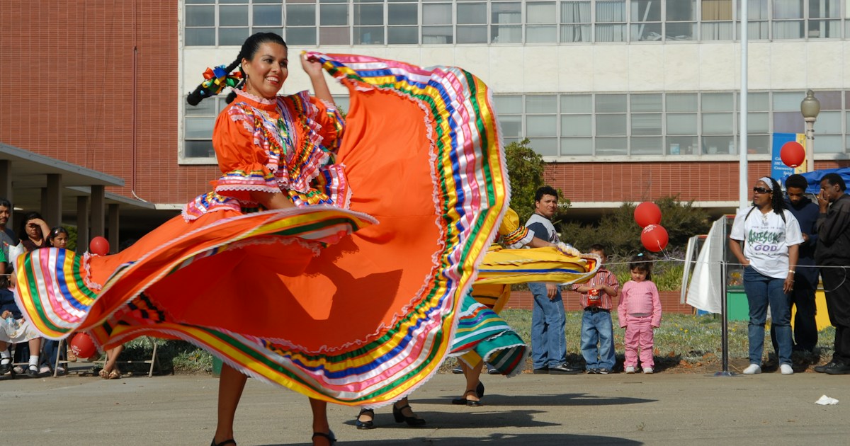 Woman dancing in orange dress by Hispanic Month woman in red yellow and blue dress holding red and yellow textile